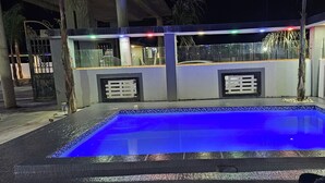 An outdoor swimming pool with a blue illuminated edge, surrounded by a concrete deck and a glass railing. - Adelina Hotel (Rustenburg)