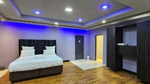 A modern hotel room with a large bed, dark wood flooring, and a walk-in closet. - Adelina Hotel (Rustenburg)