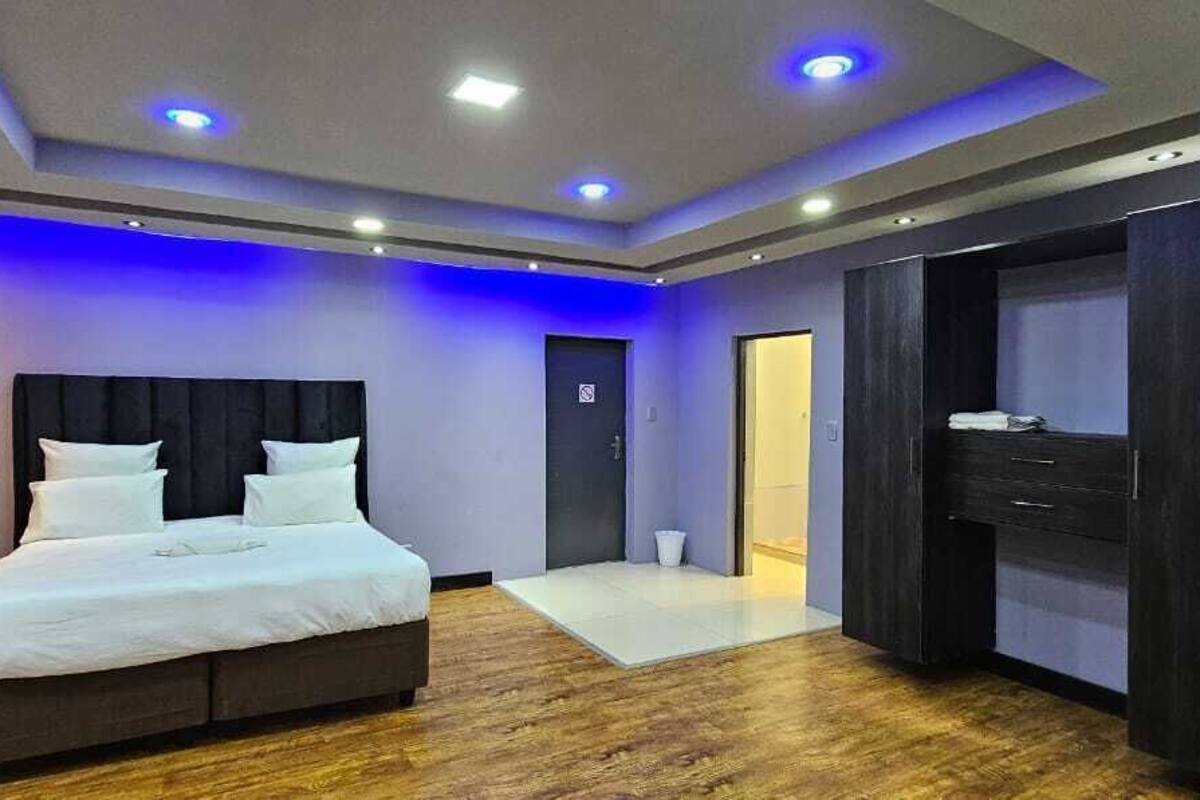 A modern hotel room with a large bed, dark wood flooring, and a walk-in closet.