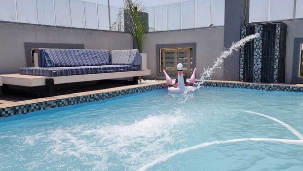 A swimming pool with a water fountain feature, a blue sofa, and a tiled wall. - Adelina Hotel (Rustenburg)