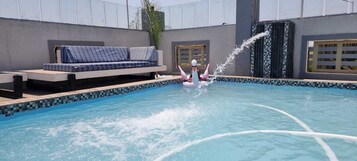 Una piscina con fuente de agua, un sofá azul y una pared con azulejos.