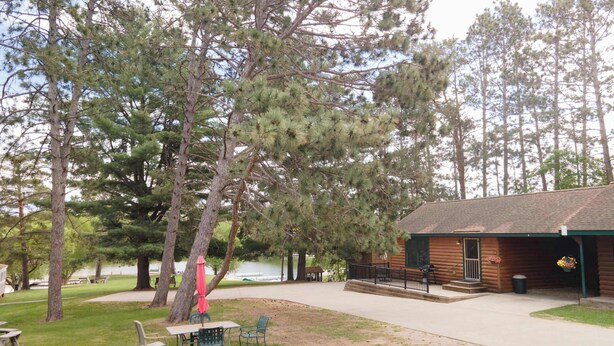 A cabin with a porch, a picnic table, and chairs in a wooded area.