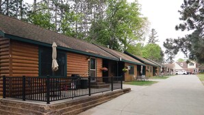 A log cabin-style building with a porch, outdoor seating, and a vehicle parked in the driveway.