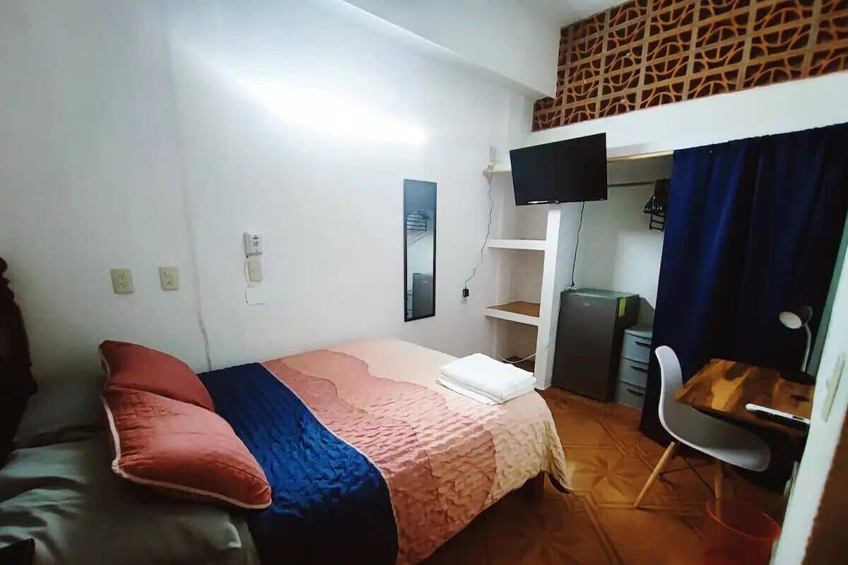 A small, compact room with a bed, a desk, a chair, and a television.