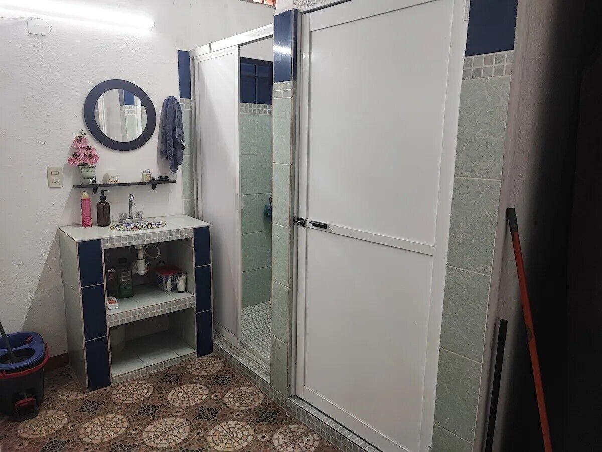 Um banheiro com piso ladrilhado, pia com espelho e box de chuveiro.
