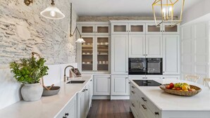 Una cocina moderna con armarios blancos, una isla central, una pared de acento de piedra e iluminación colgante.