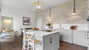 Cocina moderna con armarios blancos, una isla grande y una pared de piedra rústica.