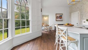 Una cocina con un ventanal grande, suelo de madera, muebles blancos y un frutero sobre la encimera.