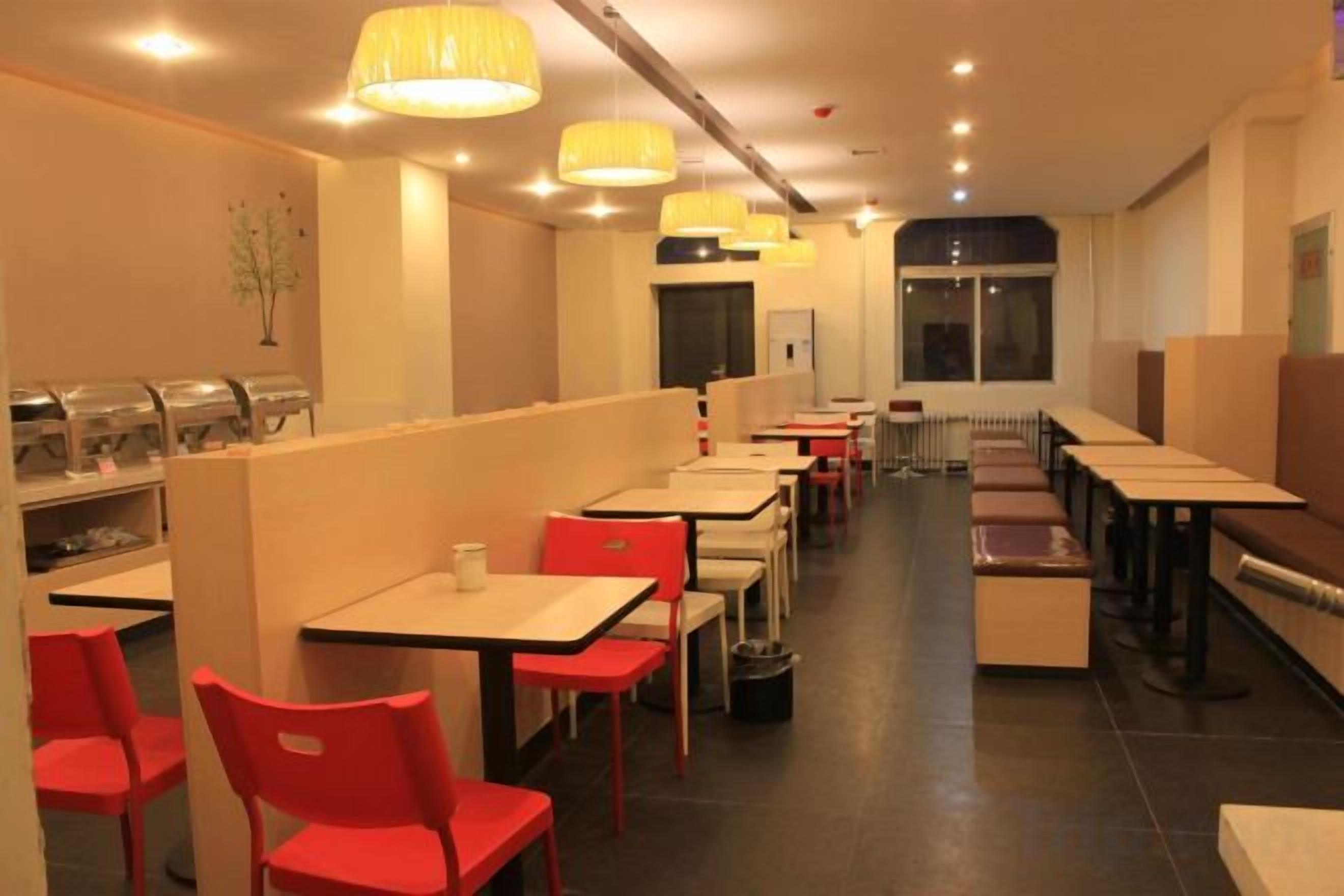 Un restaurante con varias mesas y sillas, un mostrador con dispensadores de comida y una barra alargada con asientos.