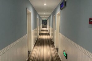 A hotel hallway with a striped carpet, white wainscoting, and a green exit sign. - Fanke Hotel (Jinan Railway Station South Square Branch ) (Jinan)