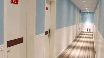 Pasillo de hotel con puertas numeradas 328 y 329, alfombra a rayas y extintor.