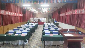 A conference room with rows of tables and chairs, a podium, and red curtains.