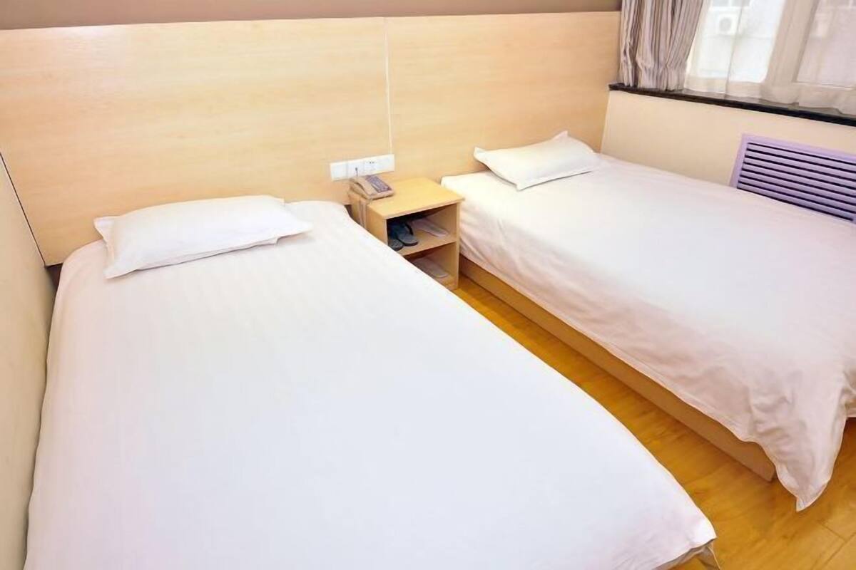 A twin room with two single beds, a bedside table with a lamp, and a window with curtains.
