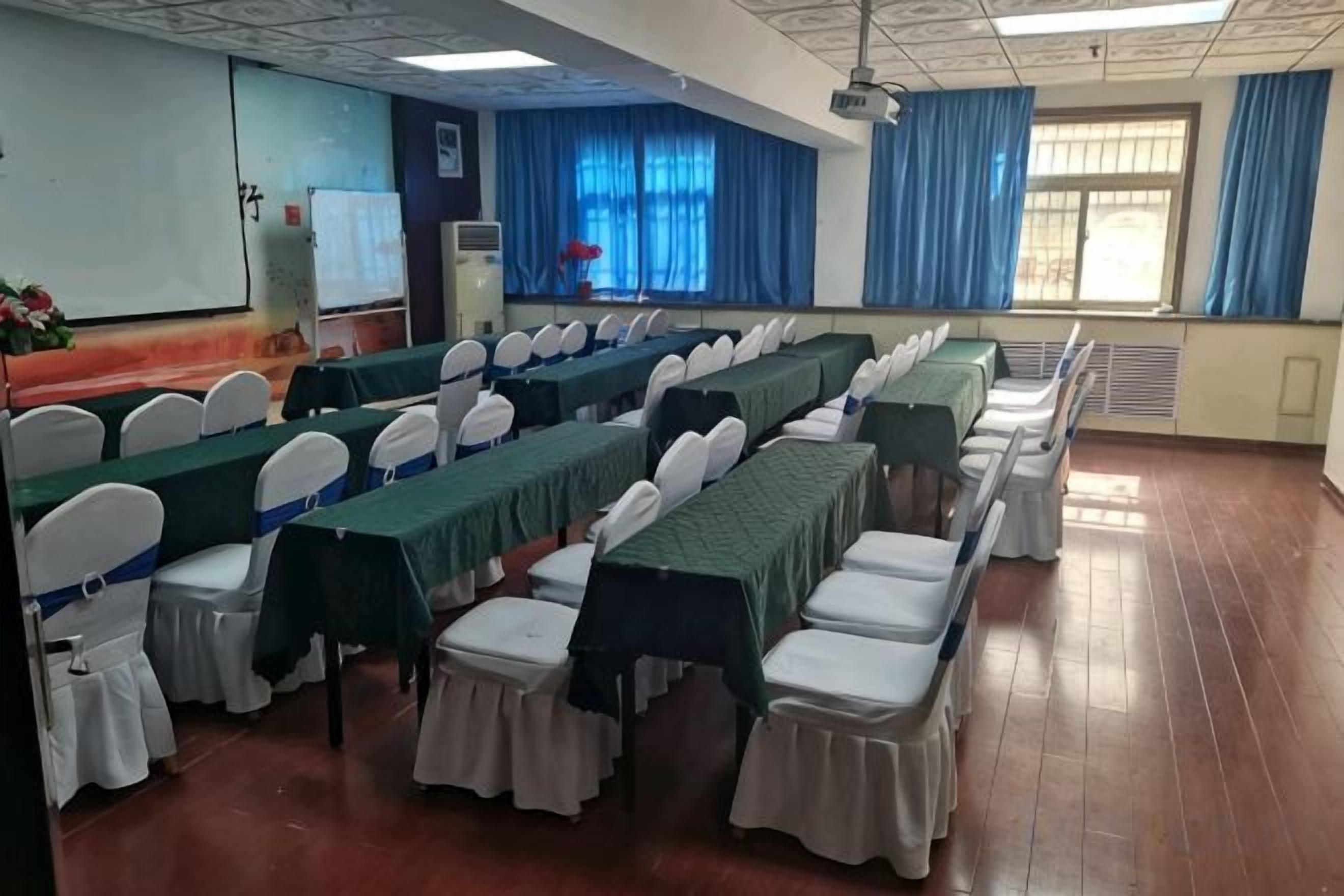 A conference room with rows of tables and chairs, a projector, and a whiteboard.