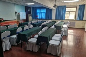 Une salle de conférence avec des rangées de tables et de chaises, un projecteur et un tableau blanc.