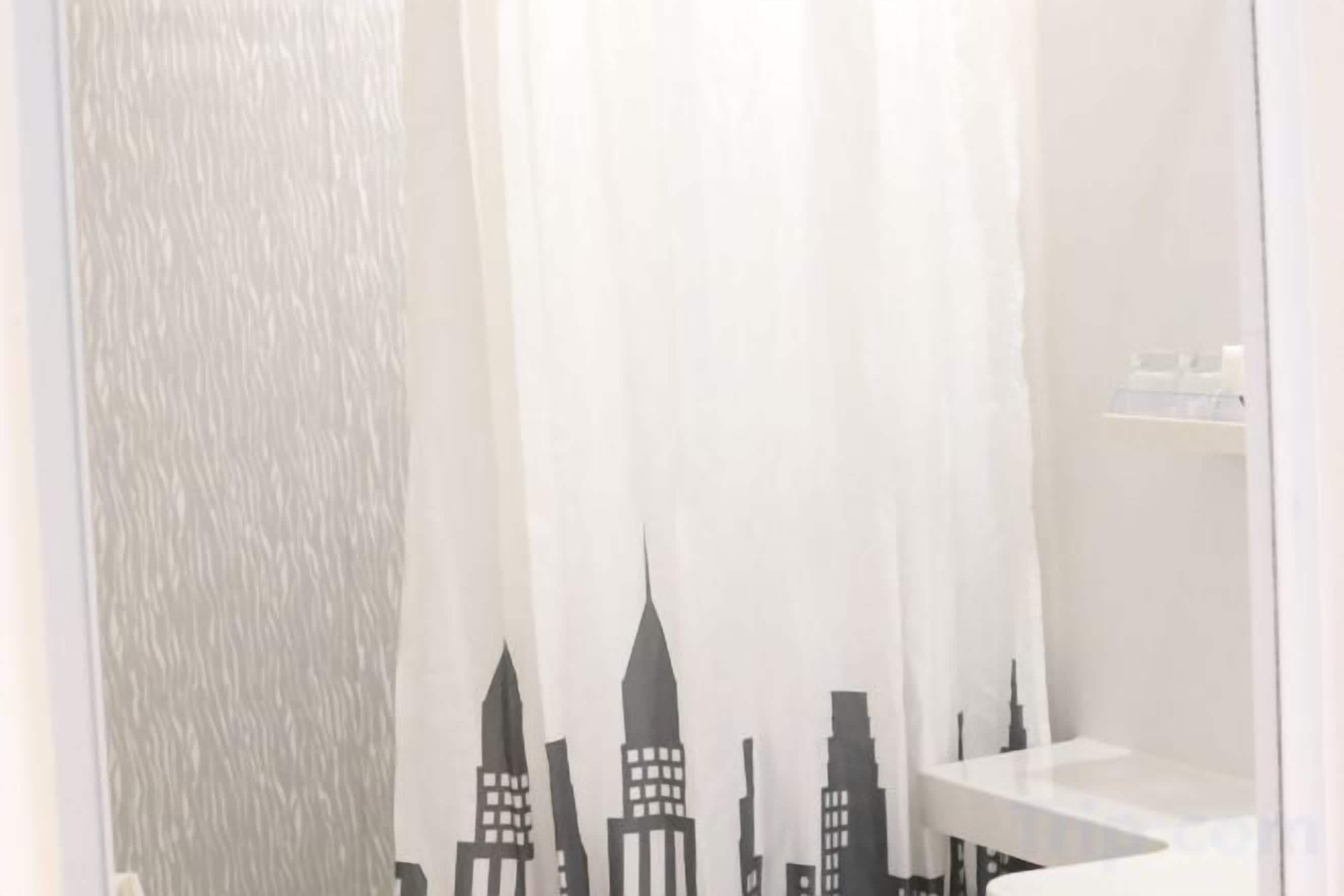A bathroom with a white shower curtain featuring a cityscape design.