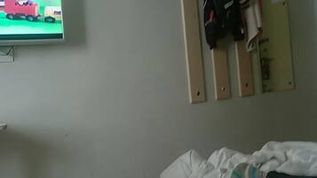 A hotel room with a bed, a television mounted on the wall, and a coat rack with hanging items.