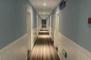 A hotel hallway with a striped carpet, white wainscoting, and a green exit sign.
