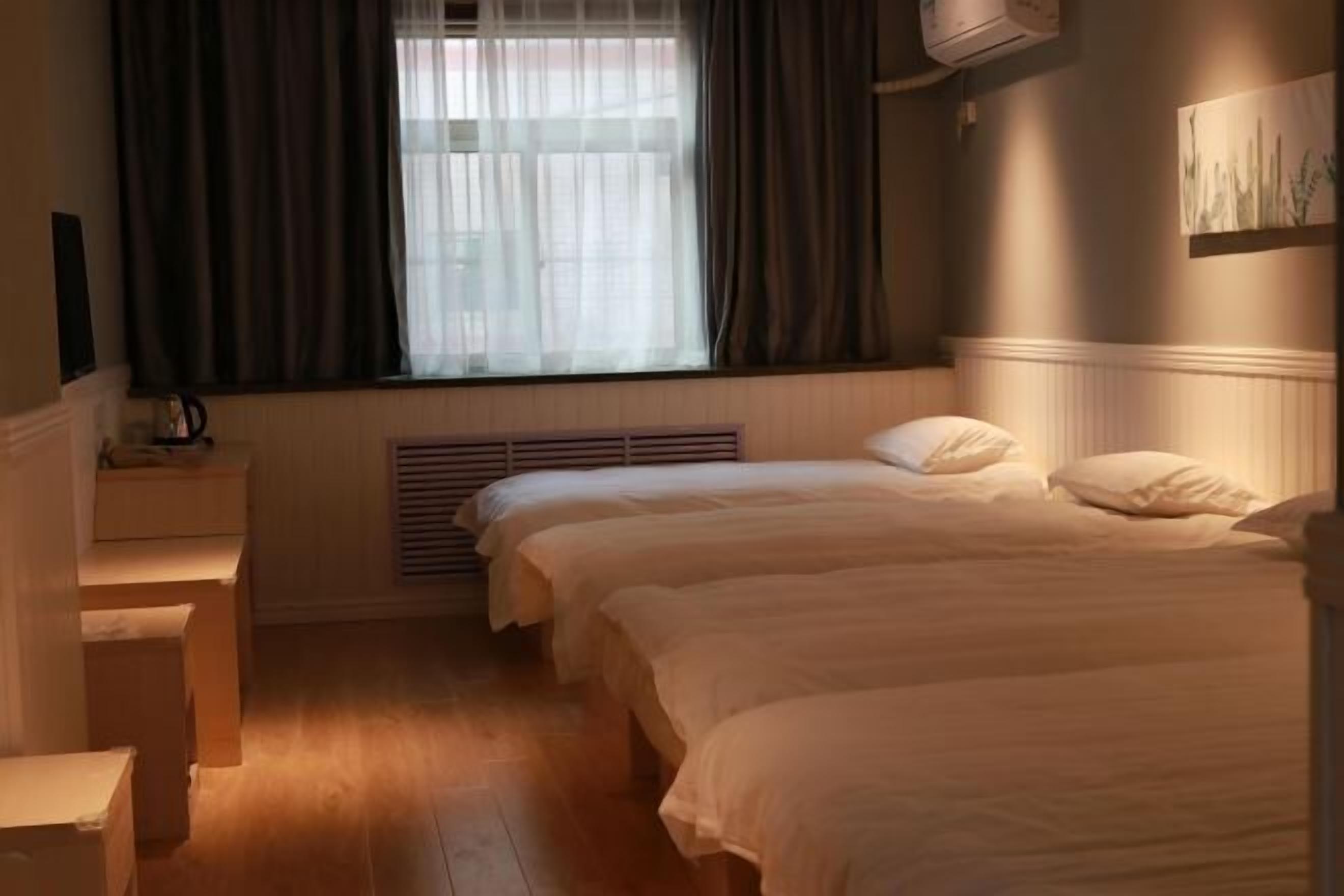 A hotel room with two beds, a window with curtains, a radiator, and a wall-mounted air conditioner.