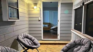 Un portico riparato con due poltrone grigie imbottite e pavimento in legno.