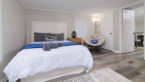 Una camera da letto con un letto, un comodino, una sedia e una porta che dà su un'altra stanza.
