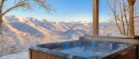 Un bain à remous au revêtement extérieur en bois, installé devant un paysage montagneux enneigé.