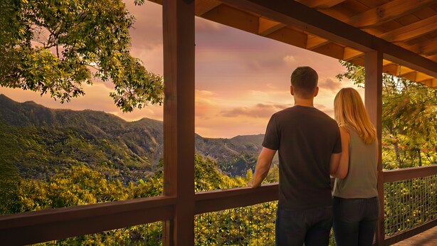 A couple standing on a wooden deck overlooking a mountainous landscape. - Hot tub, theater room w/100" tv, views, firepit, 3 king beds, porch perfection! (Maggie Valley)