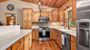 A kitchen with wooden cabinets, a stainless steel stove, a microwave, and a refrigerator. - Hot tub, theater room w/100" tv, views, firepit, 3 king beds, porch perfection! (Maggie Valley)
