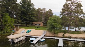 A lakeside dock with boats, a house, and surrounding trees. - 2BR 1BA Cabin #8 at Riverside Point Resort (Park Rapids)