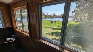 A room with a large window overlooking a grassy area with a dock and a boat. - 2BR 1BA Cabin #8 at Riverside Point Resort (Park Rapids)