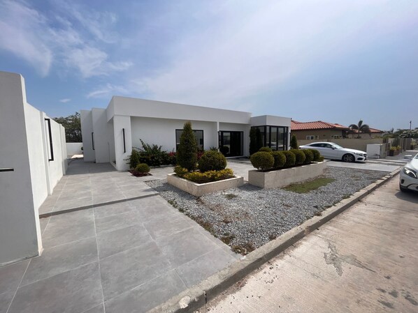 A modern building with a clean, white exterior, a driveway, and a parking area with two cars.