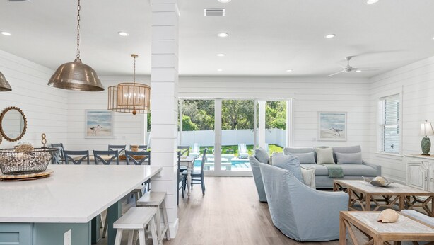 A spacious kitchen with a large island, dining area with chairs, and a view of a pool and garden. - Encore: New build! Beach access! (Santa Rosa Beach)