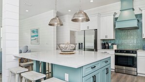 A kitchen with a large island, white bar stools, a hanging light fixture, and a blue accent wall. - Encore: New build! Beach access! (Santa Rosa Beach)