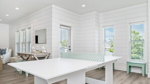 A modern kitchen with white cabinetry, a large white table, and a view of the outdoors through large windows. - Encore: New build! Beach access! (Santa Rosa Beach)
