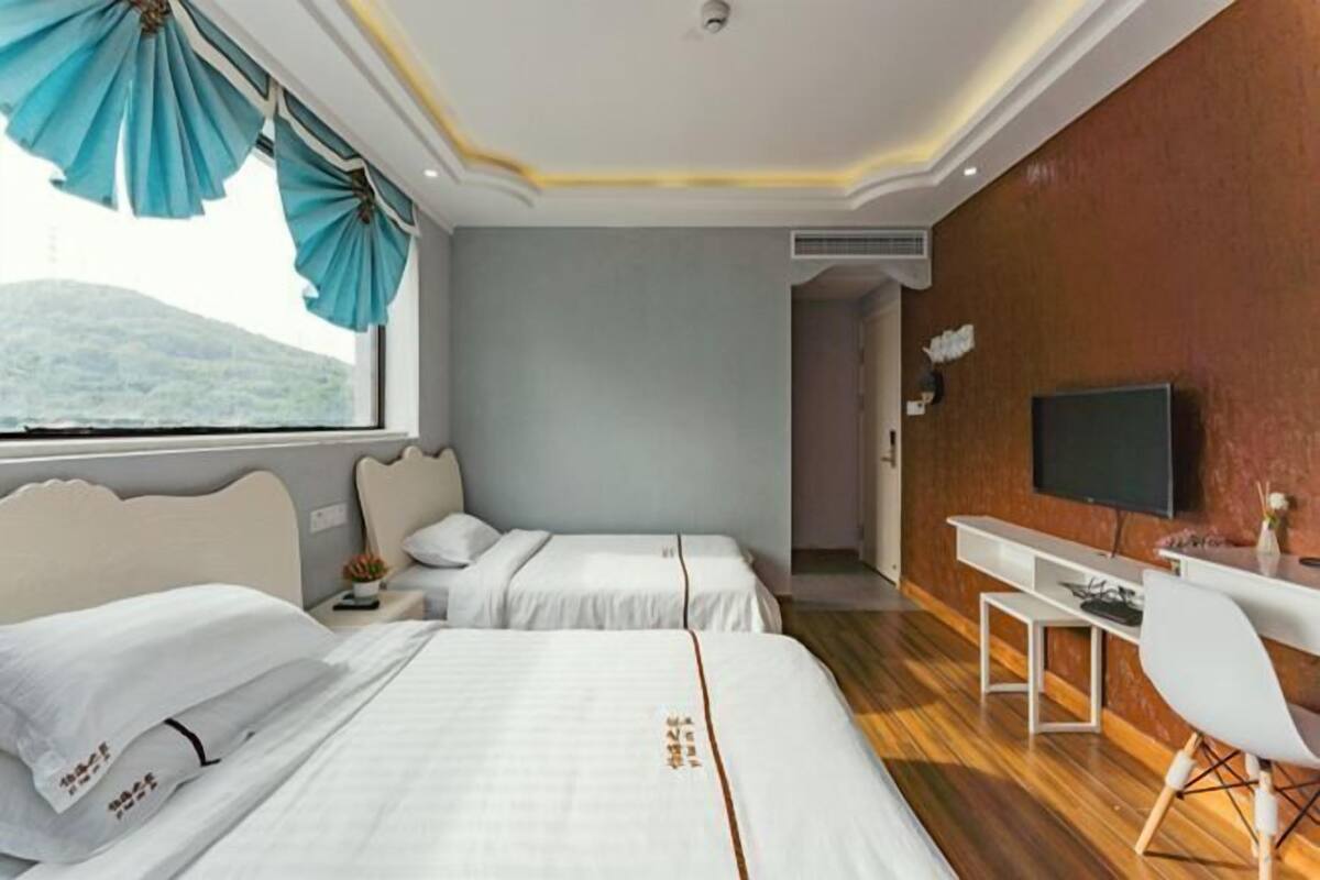 Ein Hotelzimmer mit zwei Betten, einem Schreibtisch, einem Stuhl, einem Fernseher und Blick auf einen Berg.