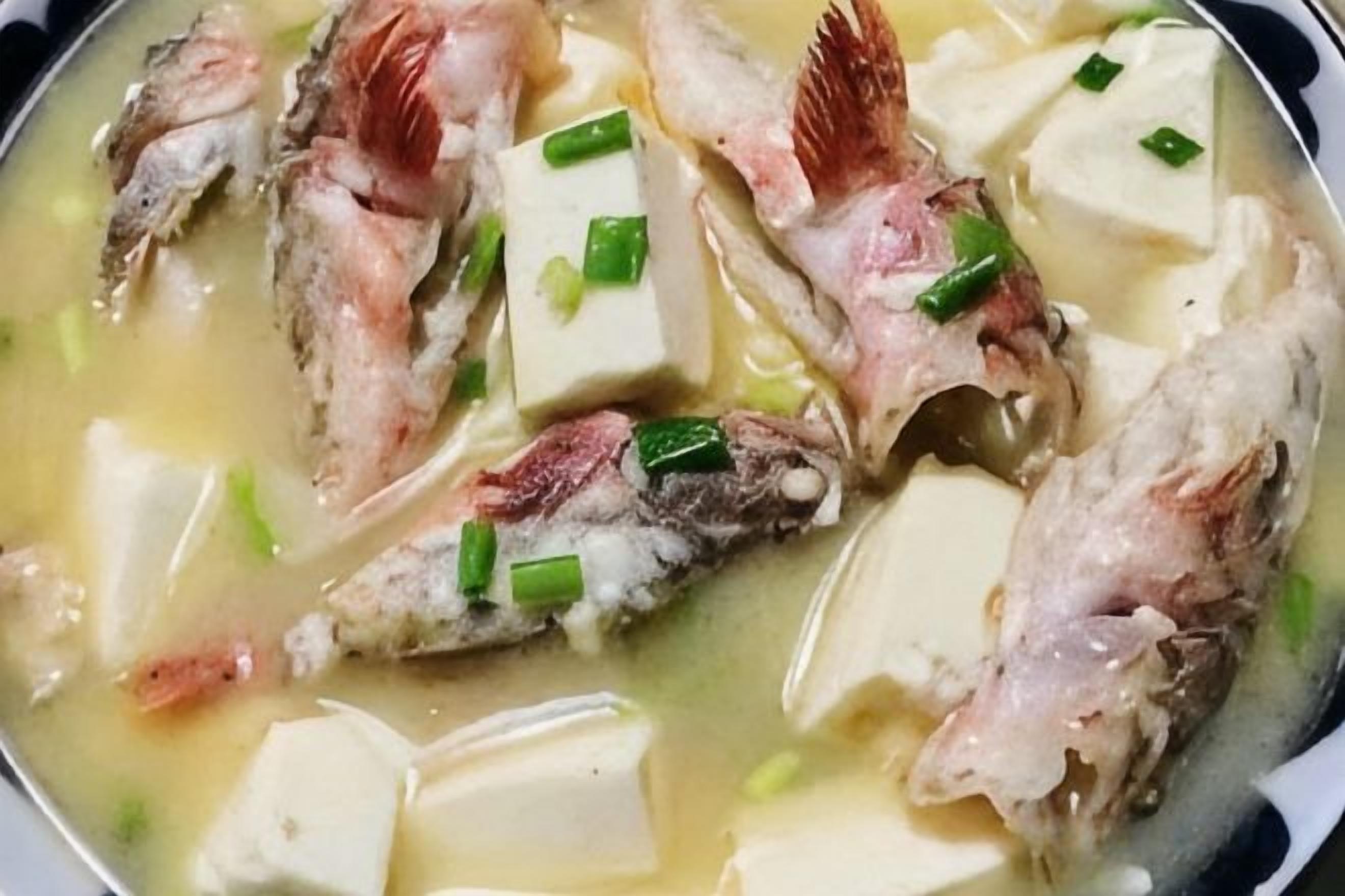 A dish with fish and tofu in a broth, garnished with green onions.