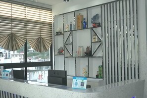 A reception desk with a computer, a glass display case with various items, and a window with blinds. - Shengsi Yihai House B & B (Shengsi)