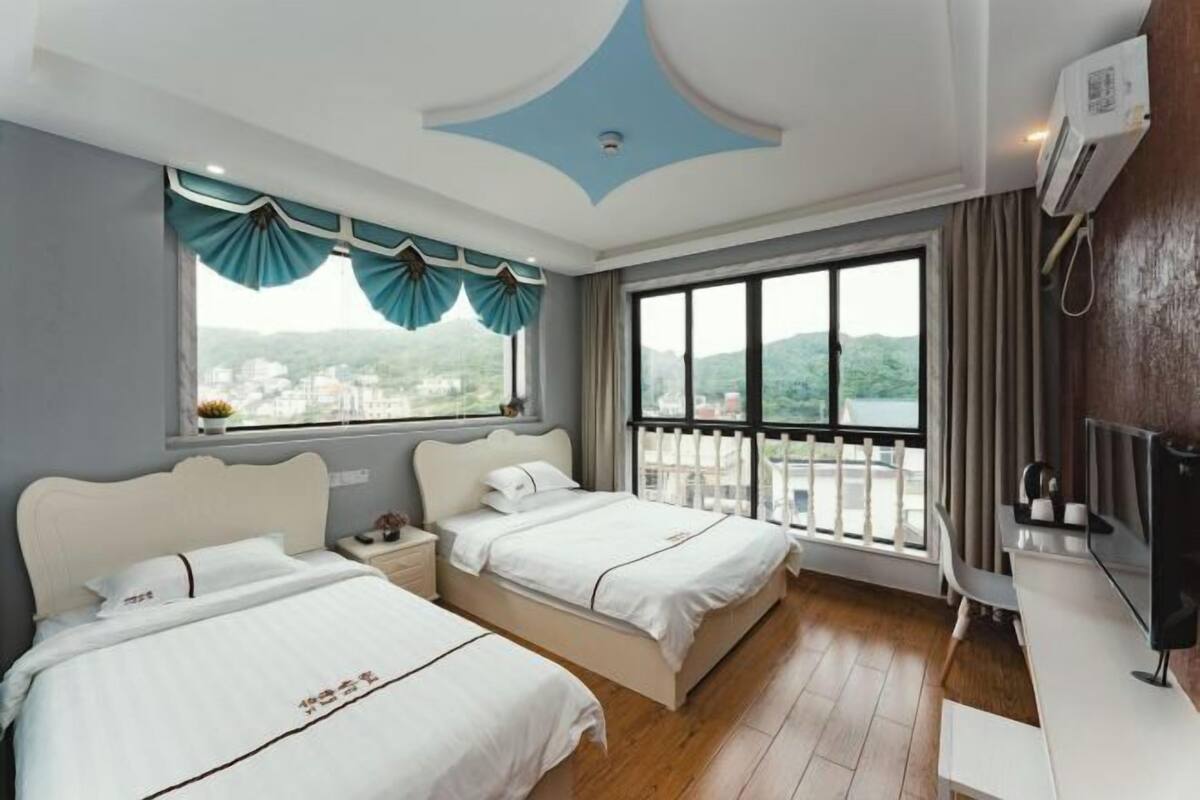 Ein Hotelzimmer mit zwei Betten, einem Fernseher, einem Schreibtisch und einem Balkon mit Blick auf die Stadt.