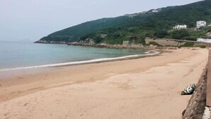 Ein Strand mit Sandküste, ruhigem Meer und einem Hügel mit Gebäuden im Hintergrund.