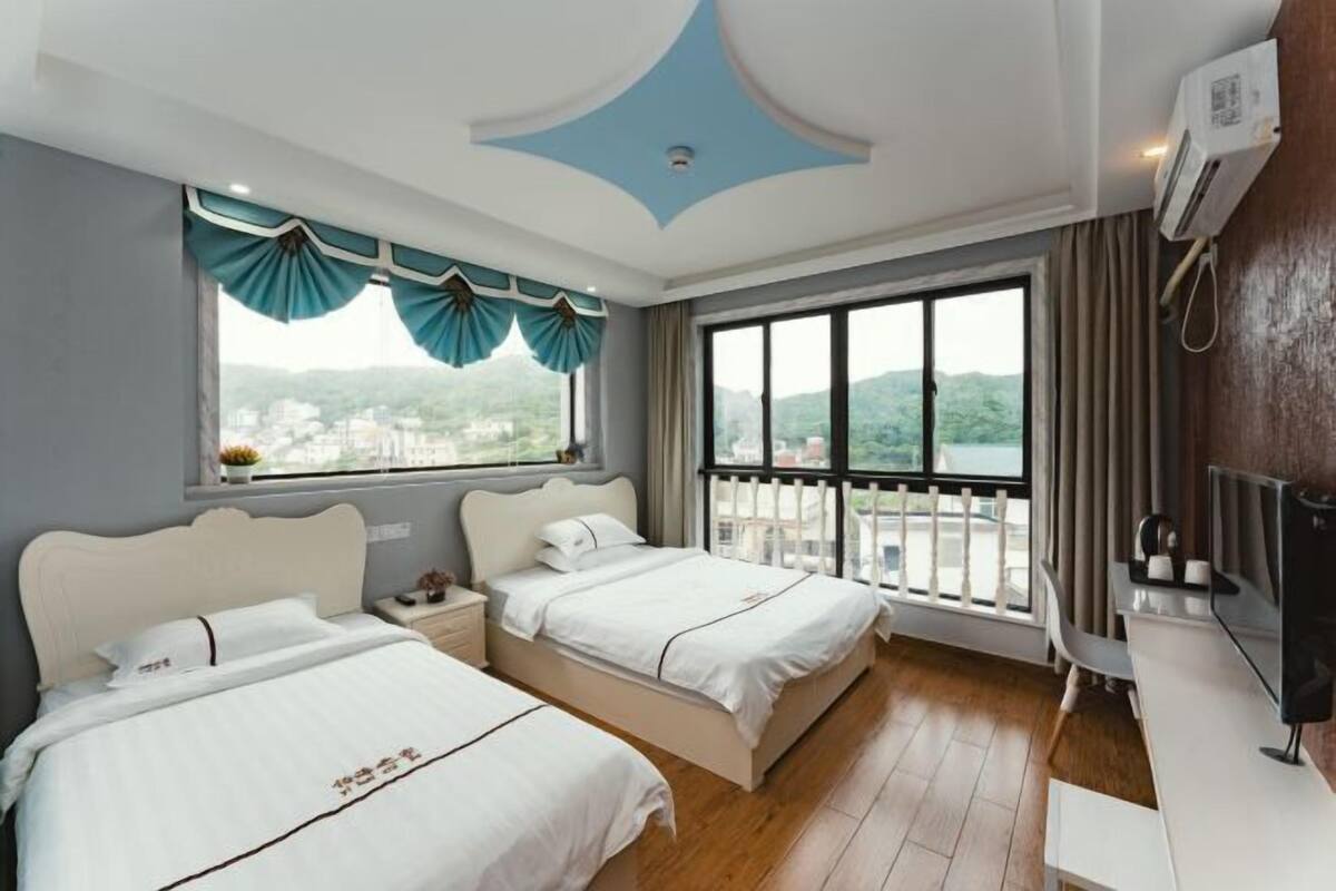 Ein Hotelzimmer mit zwei Betten, einem großen Fenster mit Vorhängen, einem Balkon und einem Fernseher.