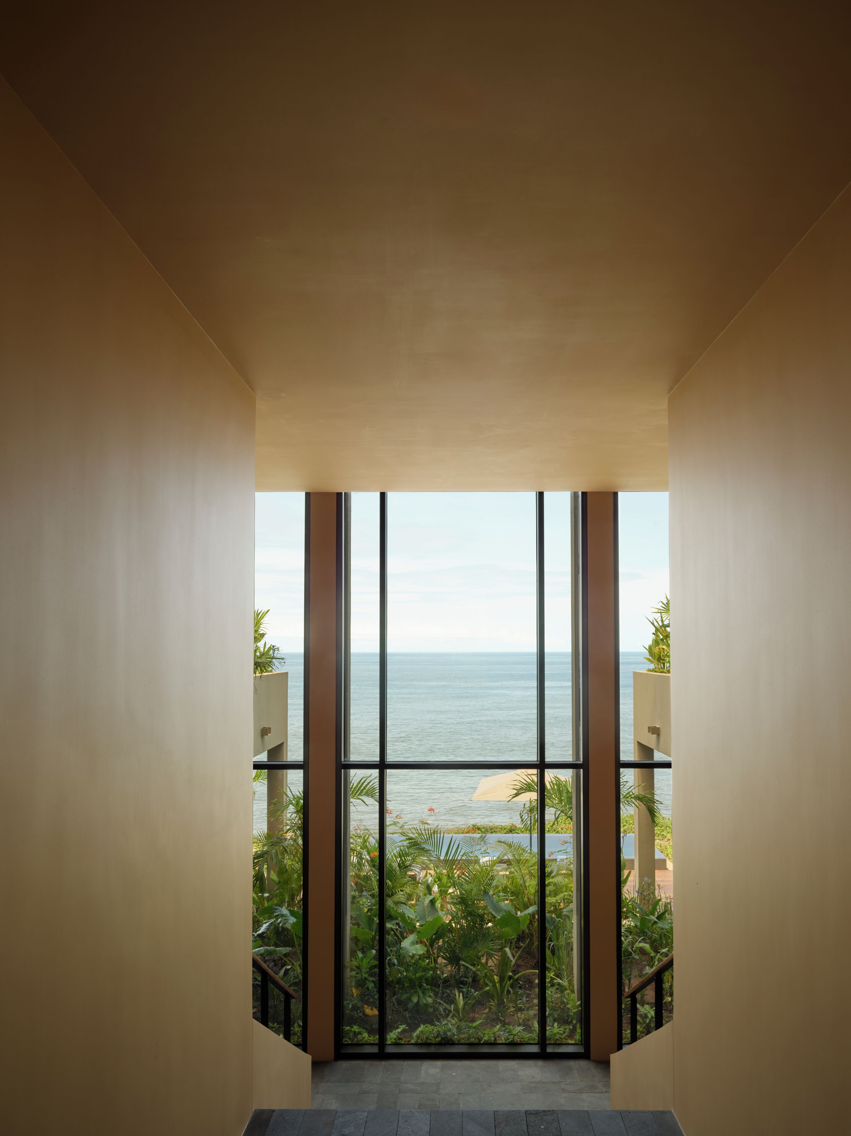 A view from a balcony with large windows overlooking a body of water and a landscaped area.