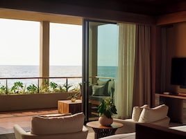 Un balcón con vista al mar, un sofá, una mesa con un florero y un televisor en la pared.