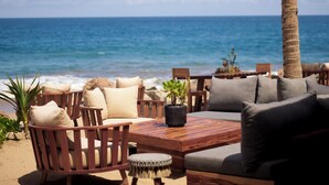 Zona relax in spiaggia con mobili in legno e cuscini, con vista sull'oceano.