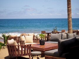 Un área de descanso frente a la playa con muebles de madera y cojines, con vista al océano.