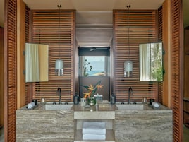 Un baño moderno con dos lavabos, paredes de listones de madera y vista al océano.