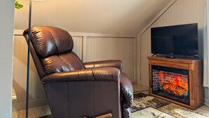 A leather recliner chair, a flat-screen TV, and a wood-burning fireplace in a room with sloped ceilings and light-colored walls. - Studio Loft #9 at Riverside Point Resort (Park Rapids)