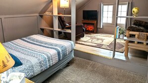 A loft-style bedroom with a bed, a fireplace, a TV, and a window. - Studio Loft #9 at Riverside Point Resort (Park Rapids)