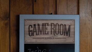 Un letrero de madera con la leyenda 'GAME ROOM' y 'AJOLA' grabado, montado en una pared.
