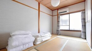 Une pièce de style japonais traditionnel, avec un sol recouvert de tatamis, un futon servant de lit, un paravent shoji et une porte coulissante donnant sur l’extérieur.
