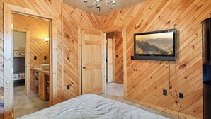A wooden-paneled room with a bed, a television mounted on the wall, and a chandelier. - Mountain Views from Sofa and Huge Deck! (Gatlinburg)